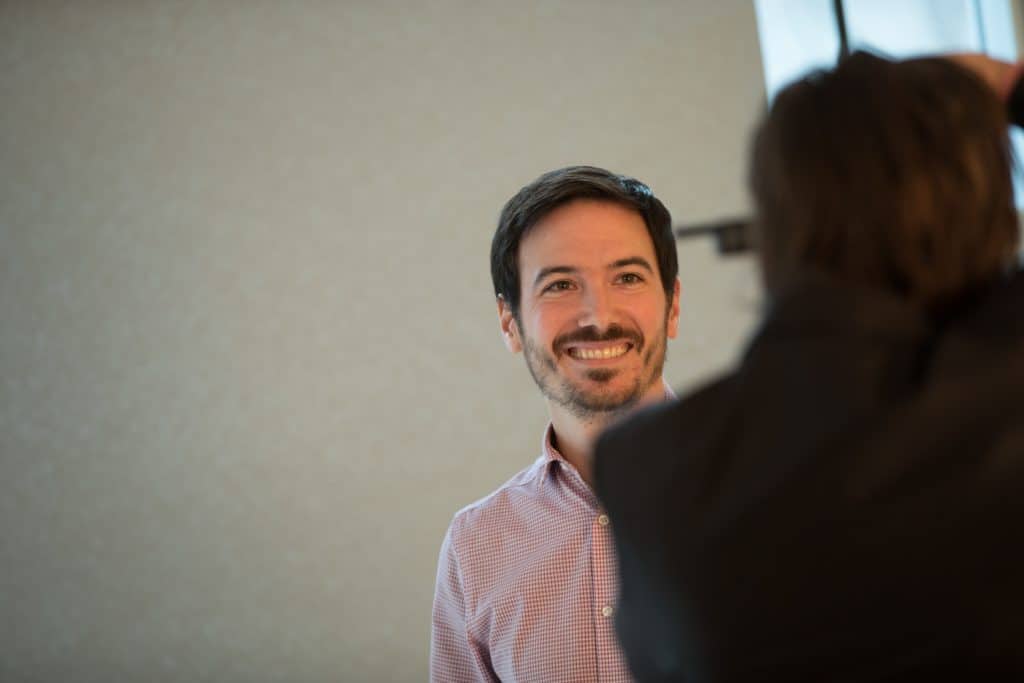 Image of man smiling standing in front of a neutral grey backdrop having corporate portrait taken by Julian Haber Image of man smiling standing in front of a neutral grey backdrop having corporate portrait taken by Julian Haber
