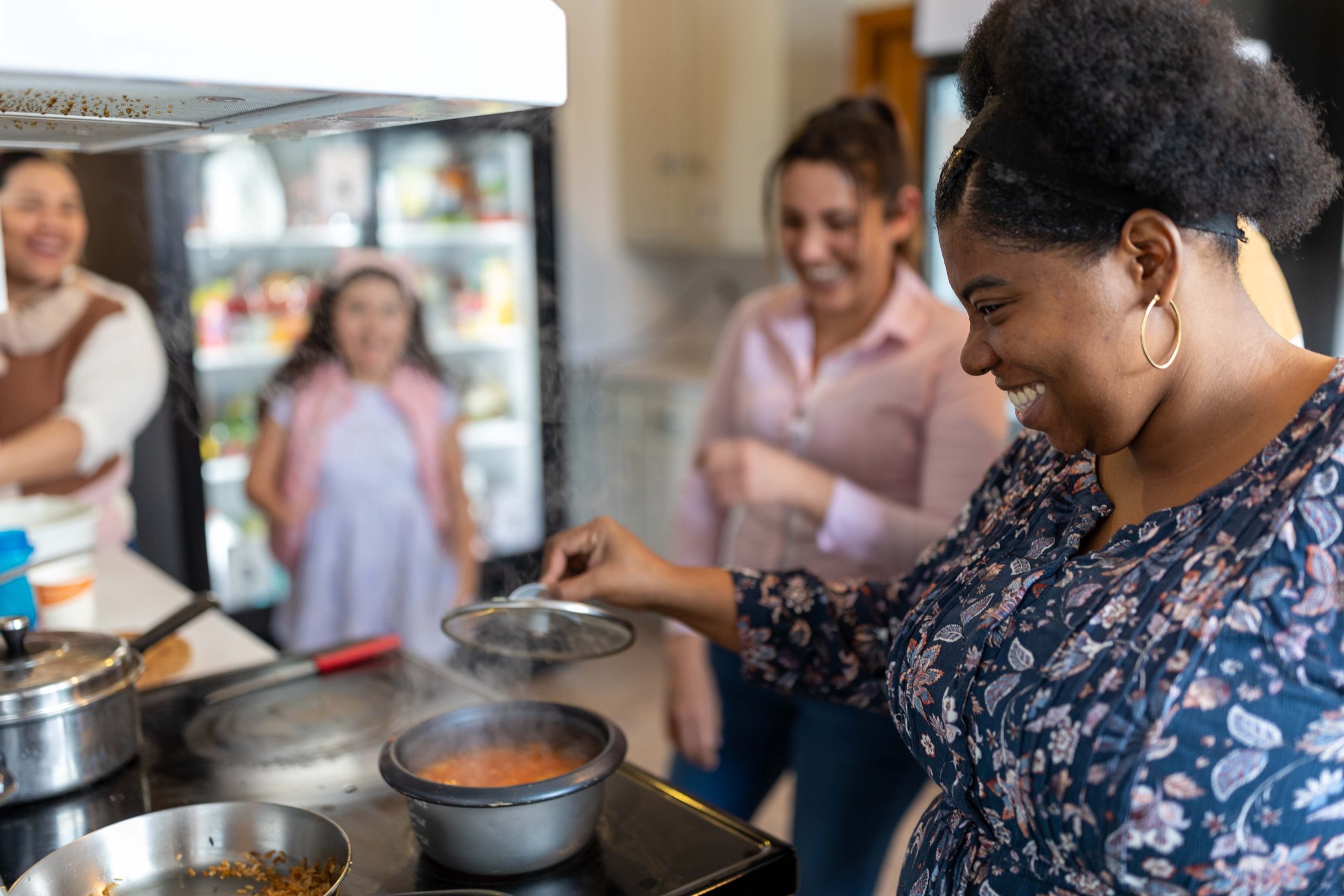 Bridge-20230328-AA8A3785 woman smiling while cooking with other people smiling in the background in a kitchen