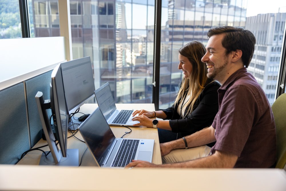 Candid workplace photography of colleagues working side-by-side in a corporate office setting.