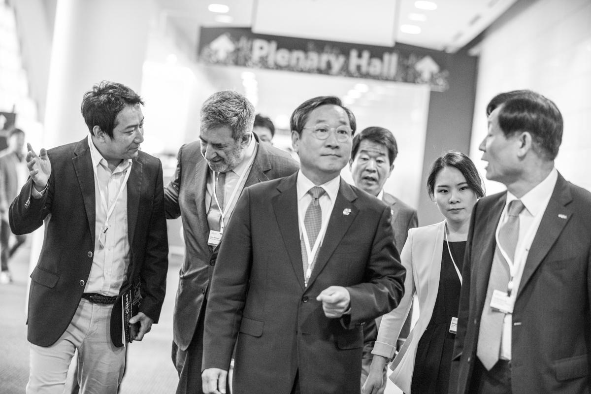 julian-haber-incheon-mayor-yoo-jeong-bok-plenary-hall-delegation-walk Incheon Mayor Yoo Jeong-bok leading a diplomatic delegation toward the Plenary Hall at the NewCities Summit in South Korea, editorial black and white photography — Julian Haber