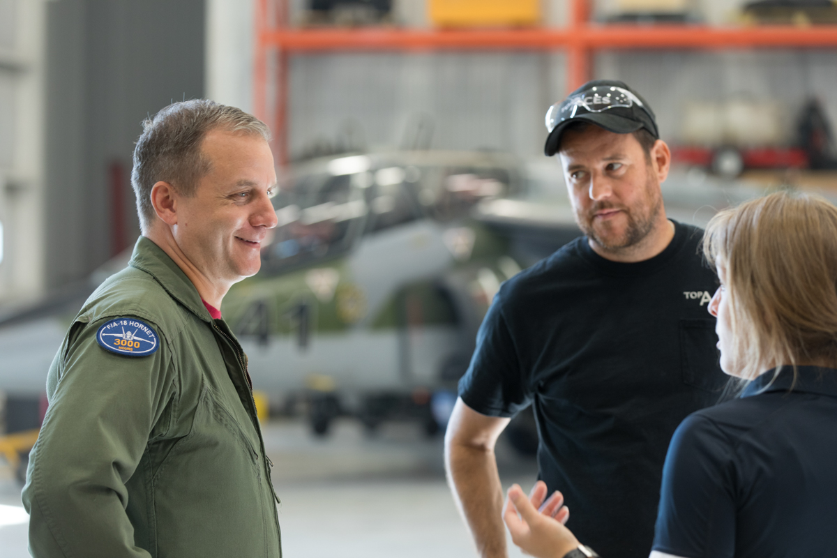 julian-haber-photography-employer-branding-montreal-24 Candid photography of a pilot in flight suit talking with a colleague in an aircraft hangar by Julian Haber