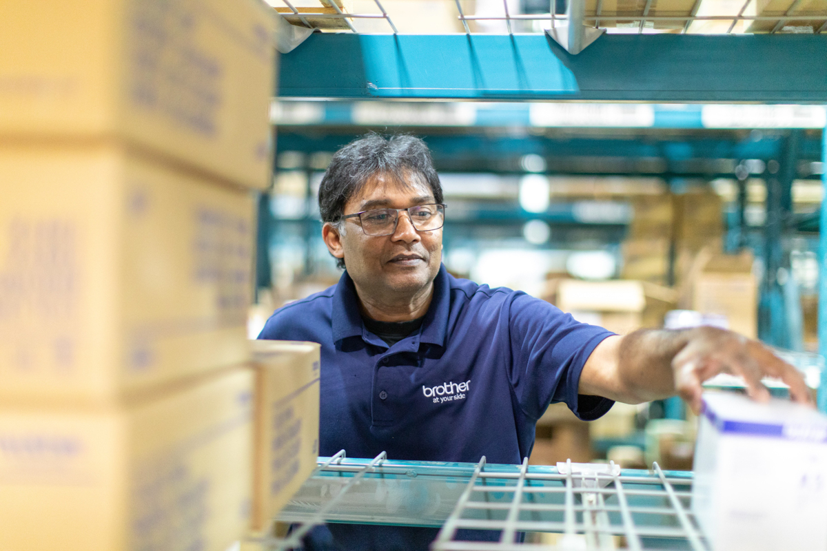 julian-haber-photography-employer-branding-montreal-30 Candid shot of a warehouse worker in a blue polo shirt picking orders from storage shelves by Julian Haber