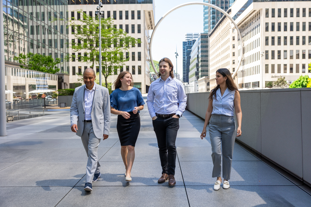 julian-haber-photography-employer-branding-montreal-52 Outdoor wide wide photography of a corporate team walking together on a sunny path in front of icon Ring sculpture at Place Ville Marie near modern architecture by Julian Haber